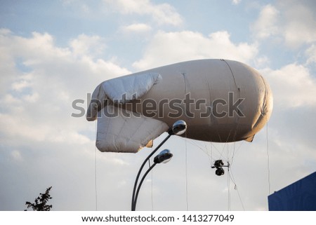 floating in the air among the clouds white airship, aircraft for advertising goods and services and high-altitude photo and video flying in the sky over the city at a low altitude