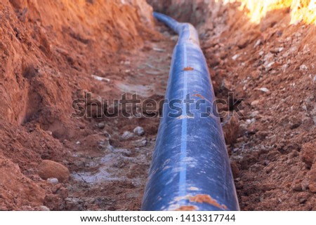 A black plastic pipe with a blue stripe lies in a dug trench to supply water to the house. Royalty-Free Stock Photo #1413317744