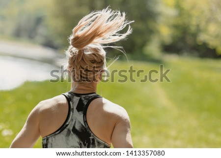Back view photo of young blonde girl wearing sportswear running in the nature, by the river in the morning. Sunny weater.  Healthy lifestyle and sport concept