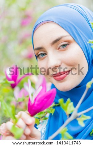 Portrait of beautiful young woman with blue eyes wearing blue hijab in blooming magnolia in park in the sunset. picture
