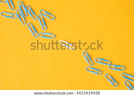 Top view photography of blue paper clips with center white isolated on yellow background. Teamwork and leadership concept.
