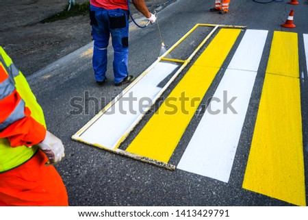 Road marking. Painting road lines. Workers draw white and yellow pedestrian lines at a pedestrian crossing.