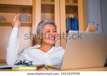 natural lifestyle office portrait of attractive and happy successful mature Asian woman working at laptop computer desk smiling confident in entrepreneur business financial success 