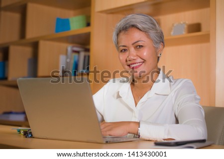 natural lifestyle office portrait of attractive and happy successful mature Asian woman working at laptop computer desk smiling confident in entrepreneur business financial success 