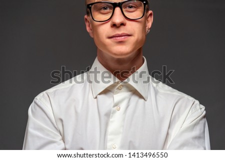 Portrait of successful self-confident young man with glasses in a white shirt posing for something on black background. Business and marketing concept
