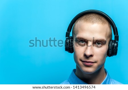 Portrait of a young handsome guy DJ in headphones and blue shirt posing against a blue background. Space for advertising