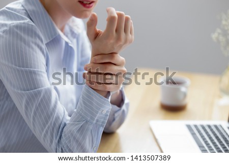Close up businesswoman holding hand feeling wrist pain from using laptop long time. Young employee suffering carpal tunnel syndrome from intensely using mouse and typing on keyboard. Computer overwork