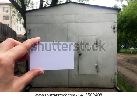 White sheet of paper in hand against the background of a silver metallic garage. Place for text.