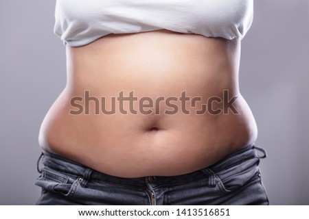 Mid Section Of A Woman With Excessive Belly Fat Against Grey Background Royalty-Free Stock Photo #1413516851