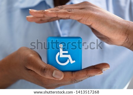 Close-up Of A Human's Hand Protecting Blue Cubic Block With Disabled Handicap Icon
