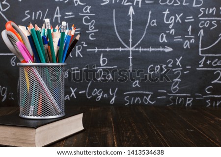 Books and stand for pens on wooden table, against the background of a chalk board with formulas. Teacher's day concept and back to school.