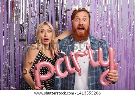 Photo of surprised girlfriend and boyfriend have astonished expressions, hold letter shaped balloons, come on party, shocked with bad organization, isolated over purple background with tinsel