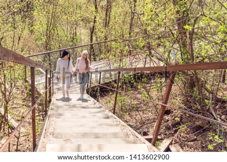 Two beautiful women climb up the wooden stairs in the forest
