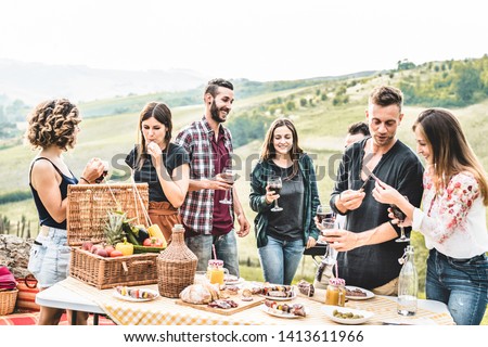 Happy adult friends eating at picnic lunch in italian vineyard outdoor - Young people having fun on gastronomic weekend tuscany tour - Friendship, summer and food concept - Focus on center guys