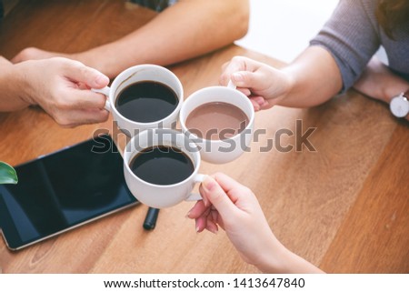 Top view image of three people clinking coffee cups on wooden table in cafe