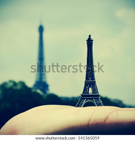 picture of someone holding a reproduction of the Eiffel Tower with the real Eiffel Tower in the background, in Paris, France, with a retro effect