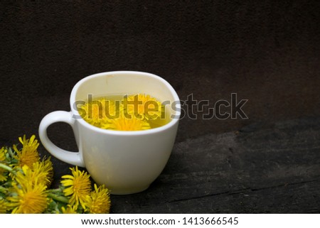Dandelion flower tea infusion in white cup close up. Herbal beverage, yellow flowers and leaves tisane on natural dark background