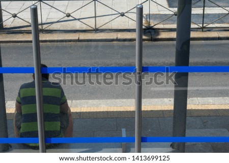 Sad man sitting at blue stripped bus stop on sunny day