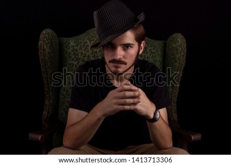 Close up of young adult male looking sinister or contemplative. Color dark tones for dramatic effect, dark and moody series. Concept image for magician in wingback chair unhappy and scheming.
