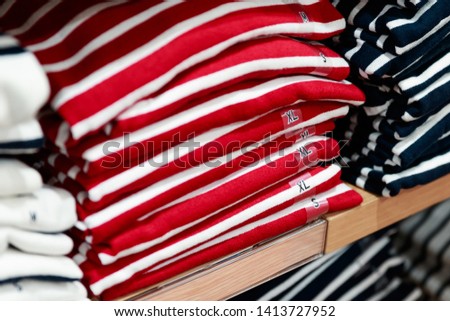 Close up of stack of folded red striped T-Shirt on a wooden shelf in a clothes shop
