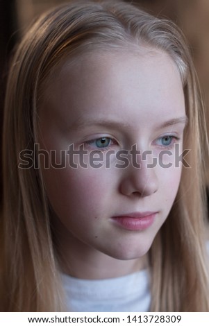 Cute Caucasian blond young girl looks  with frowning face on brown background
