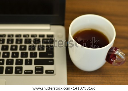 Laptop keyboard section with  a black espresso coffee cup in a white ceramic cup, setup on an office desk scenario