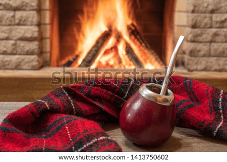 Traditional cup for mate drinking and wool scarf, near cozy fireplace, in country house, hygge, home sweet home and christmas concept.