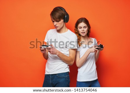cute couple in white t-shirts gamepads in the hands of video games entertainment orange background