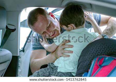 Young smiling father fastening son in safety seat in car.  Close-up picture of small boy smilling while his father helps to fasten belt on car seat. 