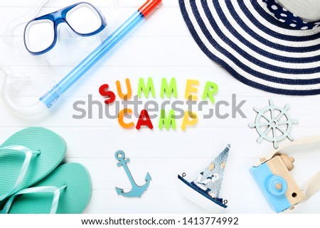 Text Summer camp with clothing, diving mask and camera on white wooden table