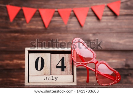 Independence Day on calendar with sunglasses and paper flags on brown wooden table