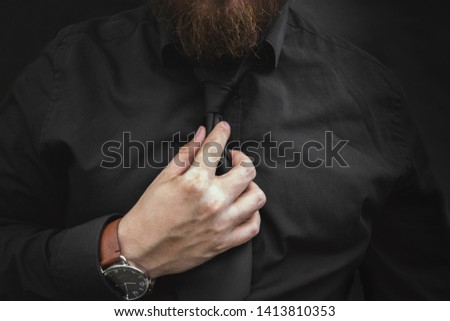 Bearded man in a black shirt adjusting his tie