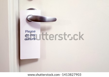 Closed white door of hotel room with please do not disturb sign