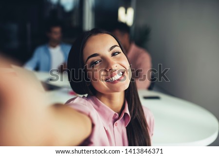 Close up portrait of cheerful hispter girl with perfect smile looking at camera and taking selfie photos during leisure time indoors, happy female teenager with brunette hair enjoying joyful mood