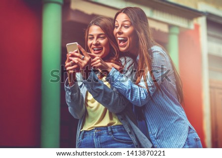 Two young women using smartphone in the street Royalty-Free Stock Photo #1413870221
