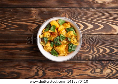 aloo gobi. Indian cuisine vegetarian curry cooked with cauliflower, potato, ginger, garlic and spices - cumin, coriander, chili and garam masala. brown woden table top Royalty-Free Stock Photo #1413870410