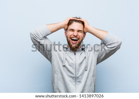 Young handsome fitness man laughs joyfully keeping hands on head. Happiness concept.