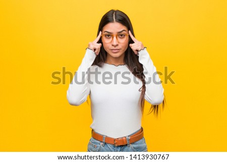 Young pretty arab woman against a yellow background focused on a task, keeping forefingers pointing head.