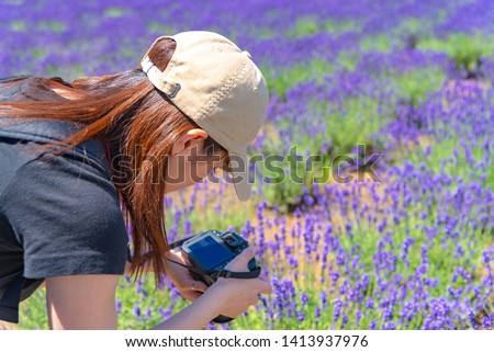 Young Japanese girl holding a digital camera and taking photo in a lavender field in summer sunny day at Furano, Hokkaido, Japan
