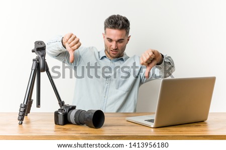 Young handsome photography teacher showing thumb down and expressing dislike.