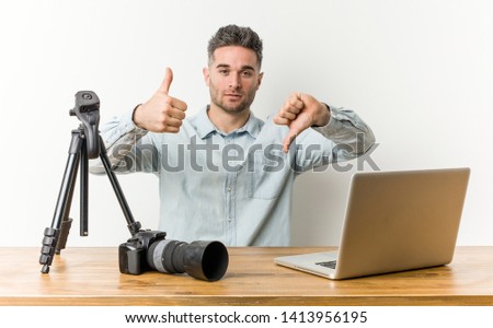 Young handsome photography teacher showing thumbs up and thumbs down, difficult choose concept Royalty-Free Stock Photo #1413956195
