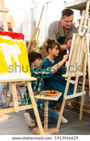 Classmates painting. Two classmates painting with teacher at the art lesson standing near drawing easel