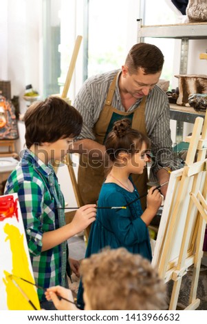 Standing near easel. Brother and his cute younger sister standing near drawing easel at art lesson