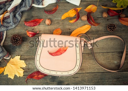 Close up a women is bag and autumn leaves on a wooden background .  Top view
