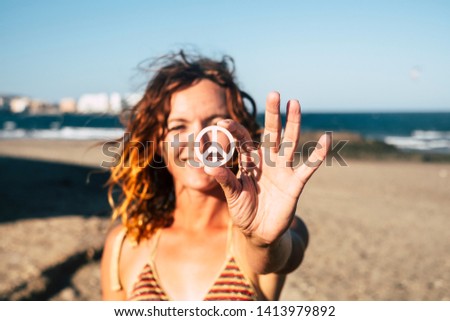 beautiful woman showing the symbol of the peace at the beach alone and isolated with the sea and the sand of the beach at the background - caucasian girl smiling and looking at the camera