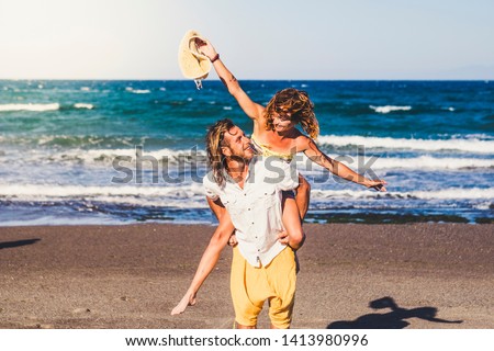 couple of beautiful adults get engaged and married together at the beach - woman on the shoulders of the man looking at him and smiling