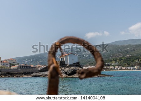 Agia Thalassini Church in a rock at the sea in Chora of Andros island through a rusty iron ring, Cyclades Greece