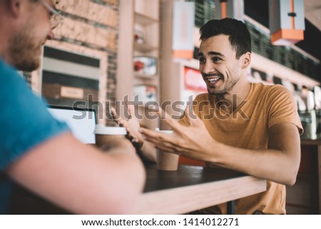 Pleasant conversation at cafeteria table during coffee break, back view of smiling young man listen talkative handsome coworker discussing new project with gesticulation, concept of communication Royalty-Free Stock Photo #1414012271