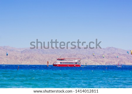 Red sea scenery landscape cruise vacation concept photography of liner and wind surfers on a vivid blue water surface and desert mountain background along Gulf of Aqaba in Jordan Middle East country