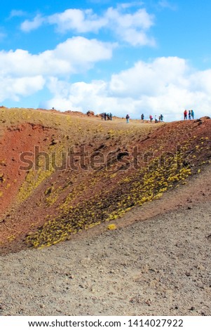 Tourists standing on the edge of Silvestri craters on Mount Etna in Italian Sicily. The amazing volcanic landscape is a popular tourist destination. Vertical photography.